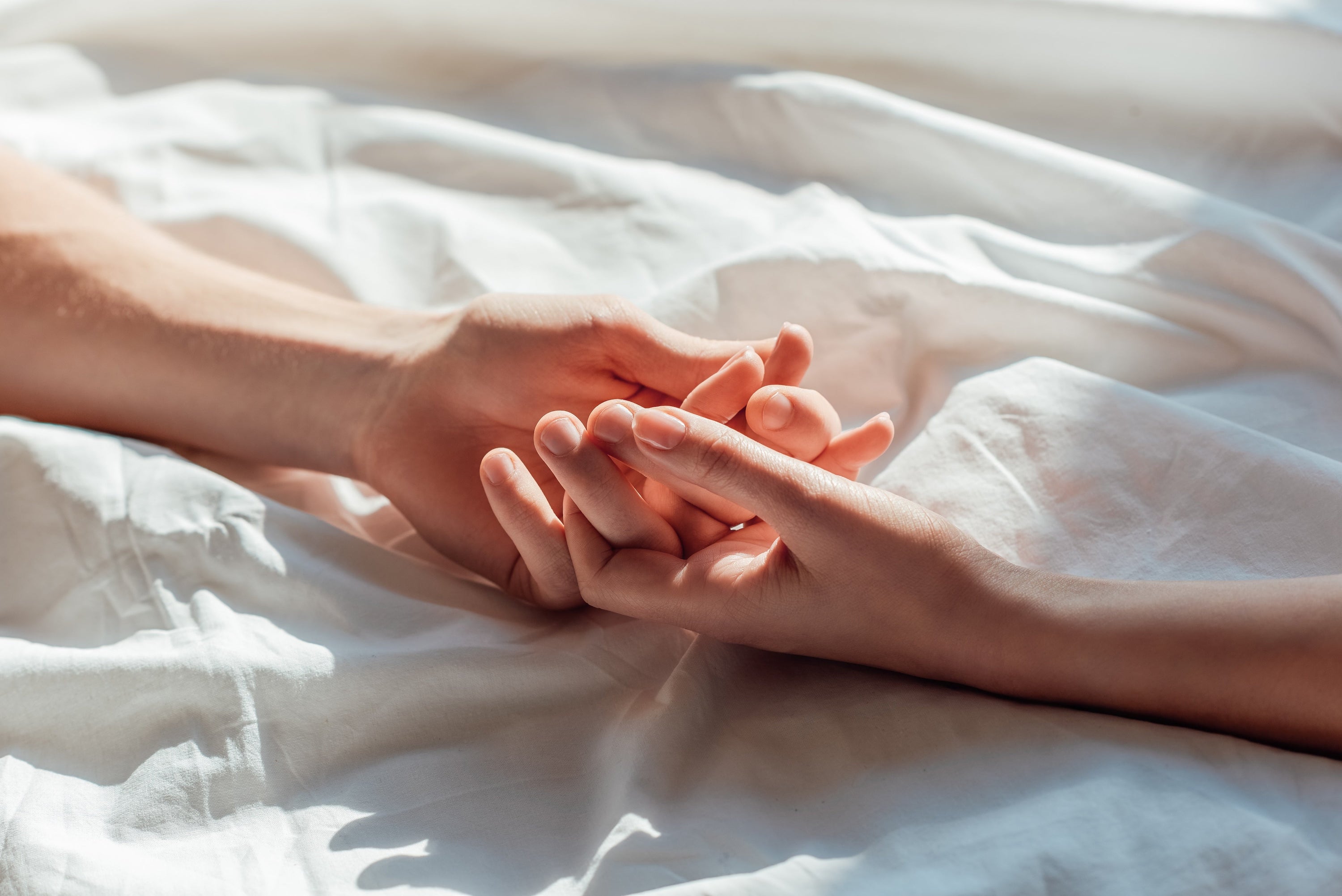 couples hands holding in bed
